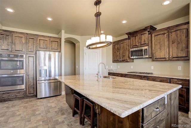 kitchen featuring pendant lighting, an island with sink, sink, stainless steel appliances, and dark brown cabinets