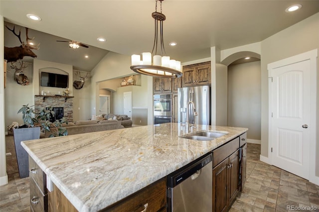 kitchen with a fireplace, decorative light fixtures, an island with sink, sink, and stainless steel appliances