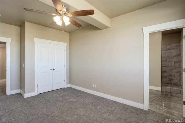 unfurnished bedroom featuring beam ceiling, dark carpet, a closet, and ceiling fan