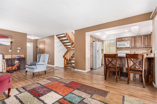 living area with light wood finished floors, a tray ceiling, stairs, and baseboards