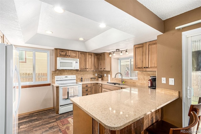 kitchen featuring white appliances, a peninsula, a sink, dark wood-type flooring, and tasteful backsplash