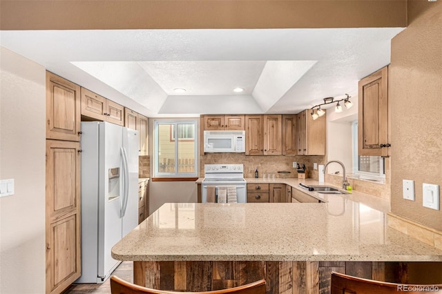 kitchen featuring a sink, white appliances, a peninsula, decorative backsplash, and light stone countertops