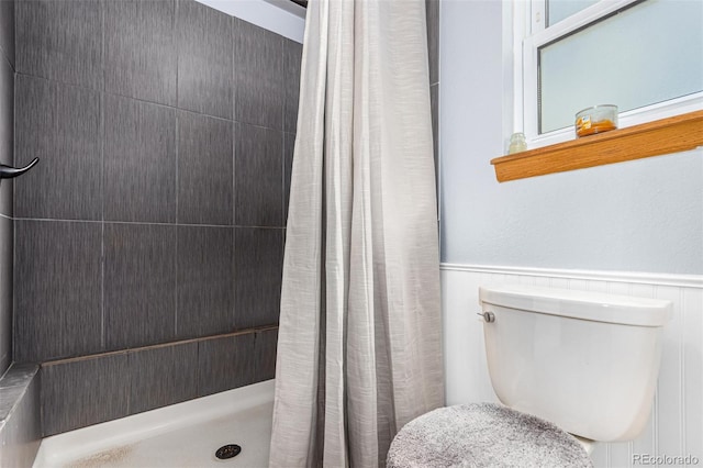 full bath with a wainscoted wall, tiled shower, and toilet