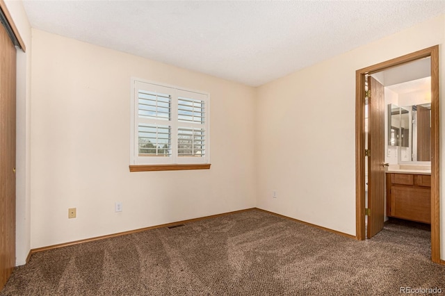 unfurnished bedroom featuring a closet, baseboards, ensuite bathroom, and carpet