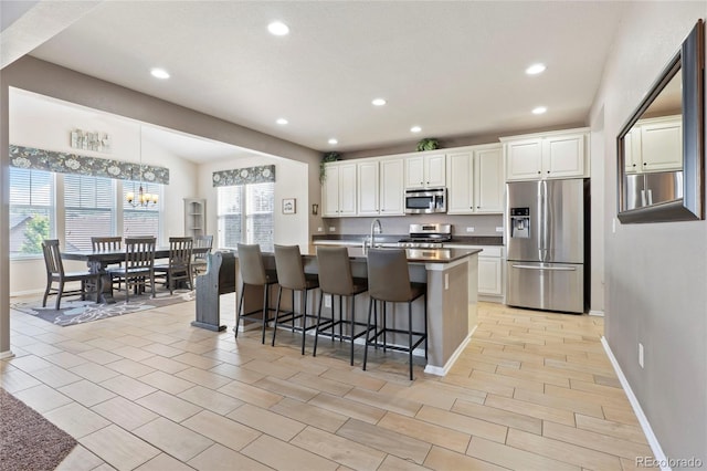 kitchen featuring a breakfast bar area, a center island with sink, recessed lighting, appliances with stainless steel finishes, and white cabinetry