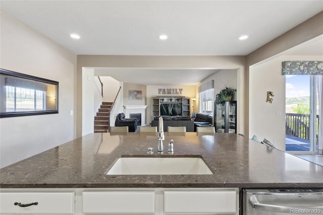 kitchen featuring open floor plan, recessed lighting, a fireplace, white cabinetry, and a sink