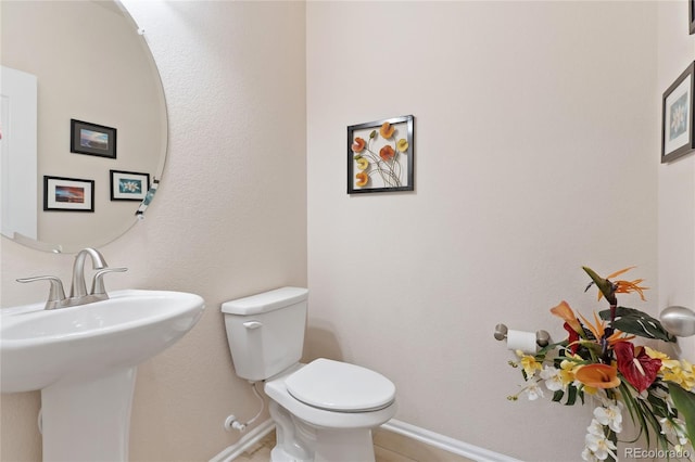 half bath with toilet, baseboards, and a sink