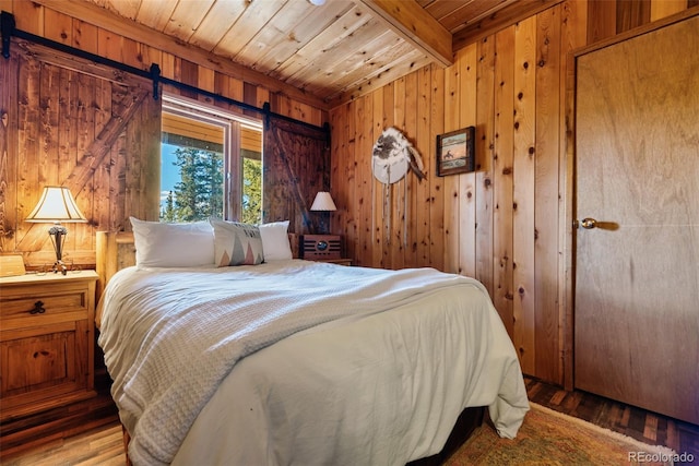 bedroom with wood walls, wood ceiling, beam ceiling, a barn door, and wood-type flooring