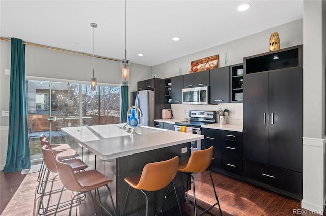 kitchen featuring an island with sink, appliances with stainless steel finishes, pendant lighting, and a kitchen bar