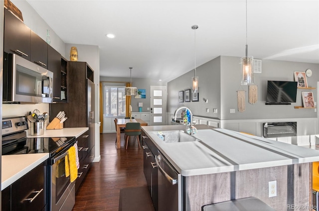 kitchen with appliances with stainless steel finishes, a kitchen island with sink, sink, and decorative light fixtures