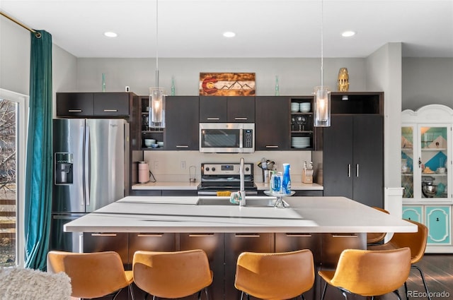 kitchen with stainless steel appliances, decorative light fixtures, an island with sink, and a breakfast bar area