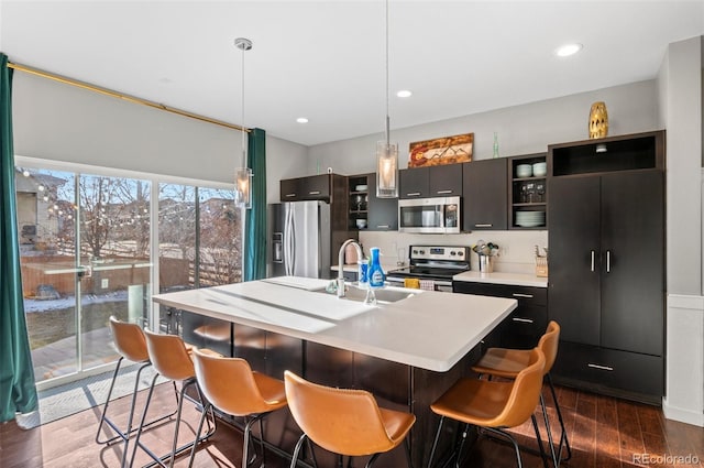 kitchen featuring sink, stainless steel appliances, decorative light fixtures, and an island with sink