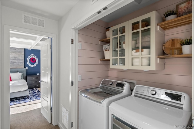 laundry area with light colored carpet, washer and dryer, and wood walls