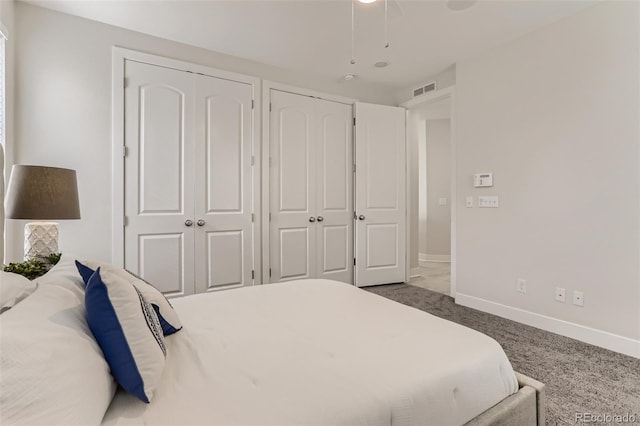 bedroom featuring multiple closets, visible vents, dark carpet, and baseboards