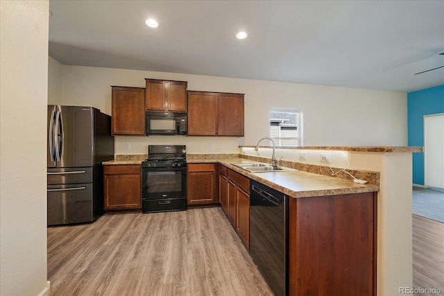 kitchen featuring black appliances, a sink, light wood-style flooring, a peninsula, and light countertops