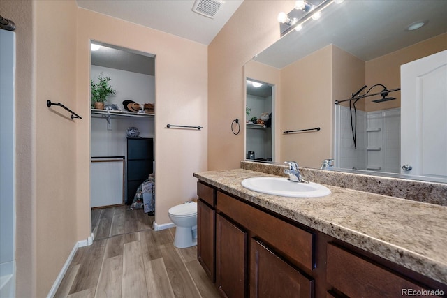 full bathroom featuring wood finished floors, toilet, a shower, a spacious closet, and vanity