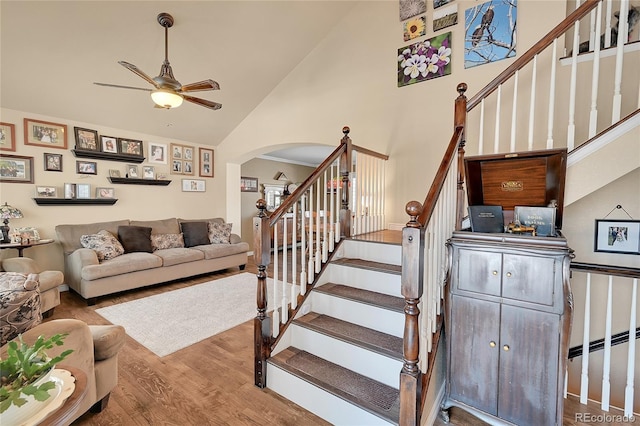 stairway with arched walkways, high vaulted ceiling, wood finished floors, and a ceiling fan