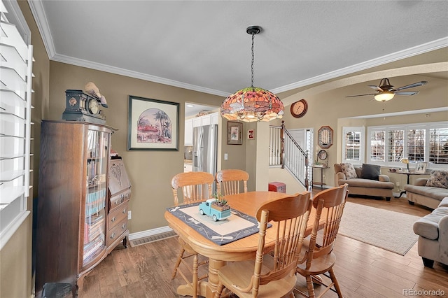 dining space featuring wood finished floors, a ceiling fan, baseboards, stairway, and crown molding