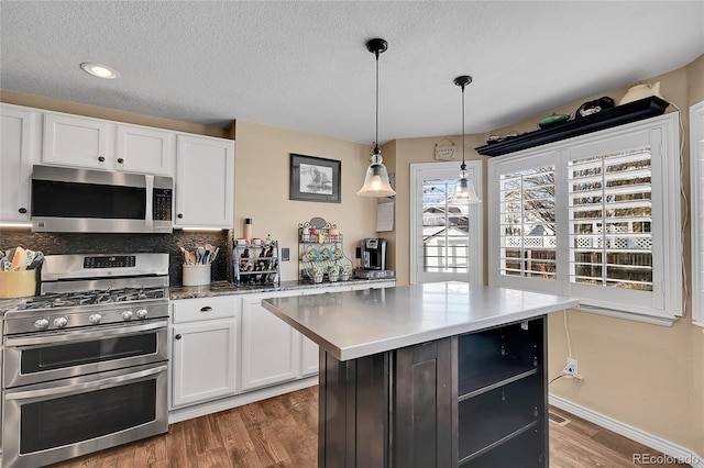 kitchen with dark wood-style flooring, a kitchen island, white cabinetry, appliances with stainless steel finishes, and decorative light fixtures