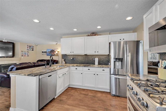 kitchen with stainless steel appliances, a peninsula, a sink, white cabinetry, and open floor plan