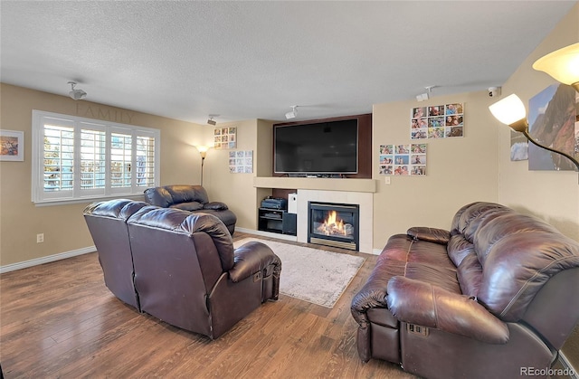 living room with a textured ceiling, baseboards, a fireplace, and wood finished floors