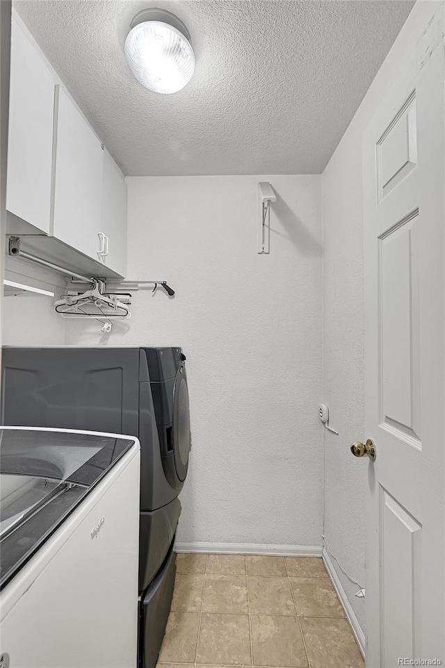 clothes washing area featuring washer and dryer, cabinet space, a textured ceiling, and light tile patterned floors