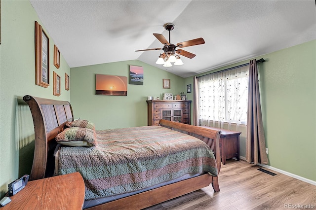 bedroom featuring lofted ceiling, light wood-style floors, a ceiling fan, a textured ceiling, and baseboards