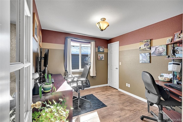 home office with light wood-style flooring, baseboards, and a textured wall