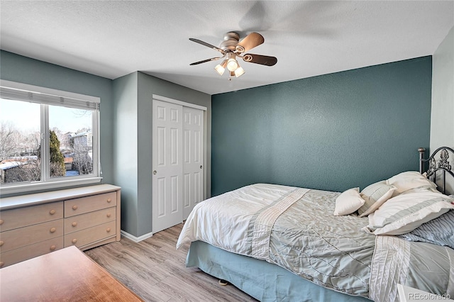 bedroom with ceiling fan, a closet, light wood-style flooring, and baseboards