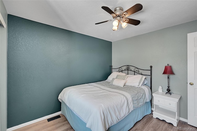 bedroom with a ceiling fan, wood finished floors, visible vents, and baseboards