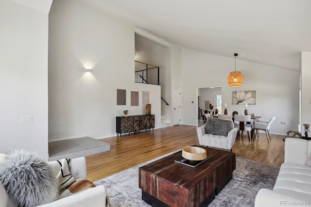 living area with high vaulted ceiling, baseboards, stairs, and wood finished floors
