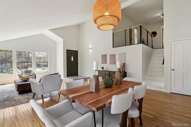 dining room featuring wood-type flooring, high vaulted ceiling, and stairs