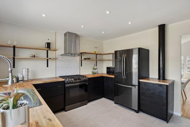 kitchen featuring wall chimney range hood, appliances with stainless steel finishes, open shelves, dark cabinets, and wood counters