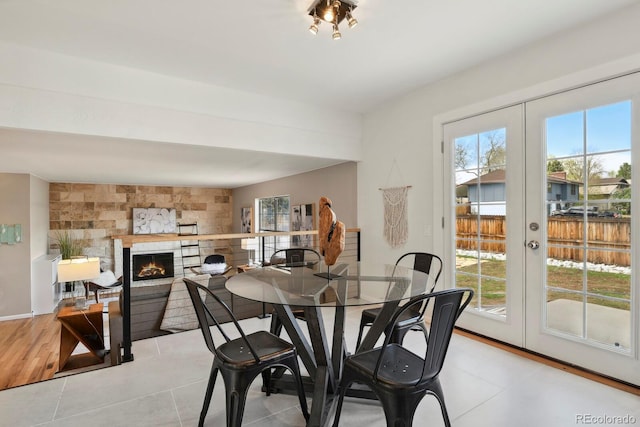 tiled dining space with french doors, a warm lit fireplace, and a wealth of natural light