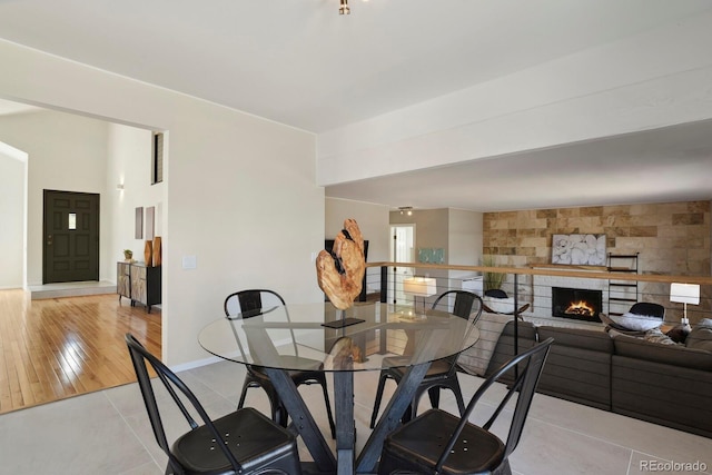 dining space featuring light tile patterned floors, baseboards, and a lit fireplace