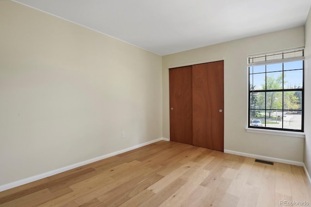 unfurnished bedroom with baseboards, a closet, light wood finished floors, and visible vents