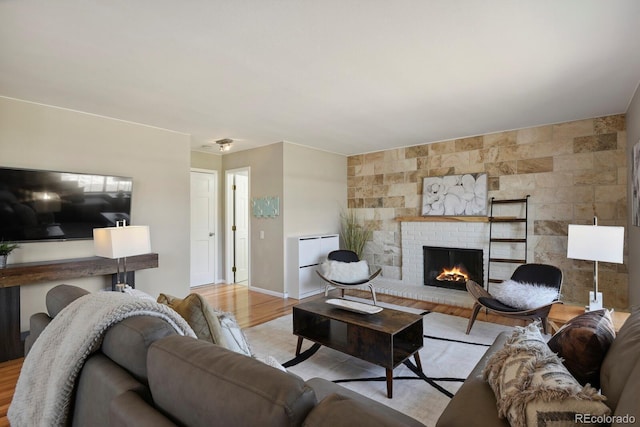 living room with a brick fireplace, baseboards, and light wood finished floors