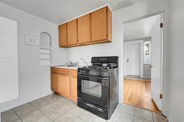 kitchen featuring black gas range oven, light tile patterned floors, and sink