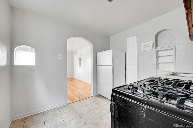 kitchen with black stove, white fridge, light tile patterned floors, and sink