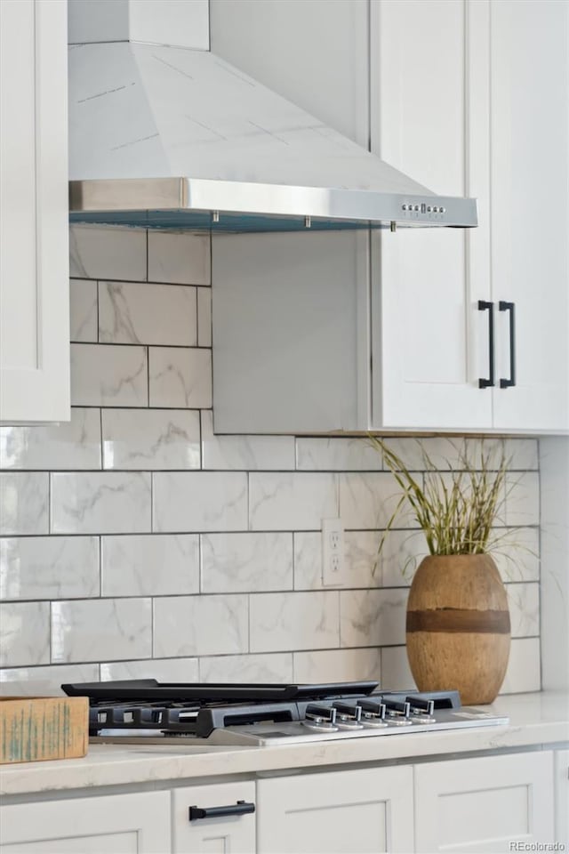 room details featuring tasteful backsplash, ventilation hood, stainless steel gas cooktop, and white cabinets