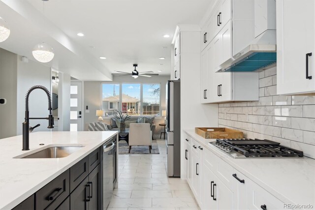 kitchen with decorative light fixtures, sink, light stone counters, stainless steel appliances, and wall chimney exhaust hood