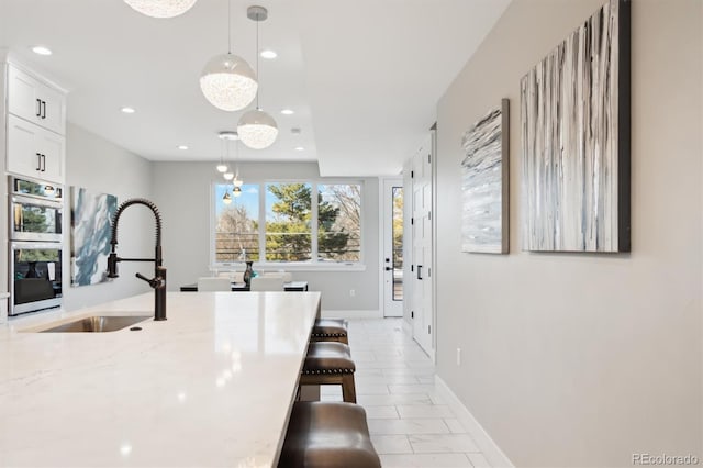 kitchen featuring sink, a breakfast bar area, decorative light fixtures, light stone countertops, and white cabinets