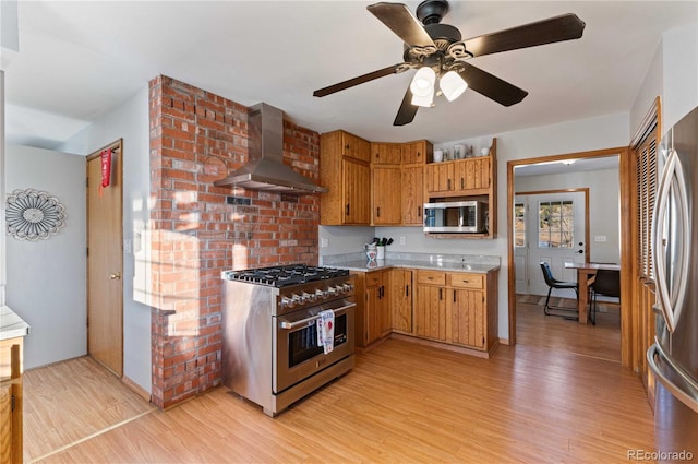 kitchen with ceiling fan, light hardwood / wood-style flooring, wall chimney exhaust hood, and appliances with stainless steel finishes