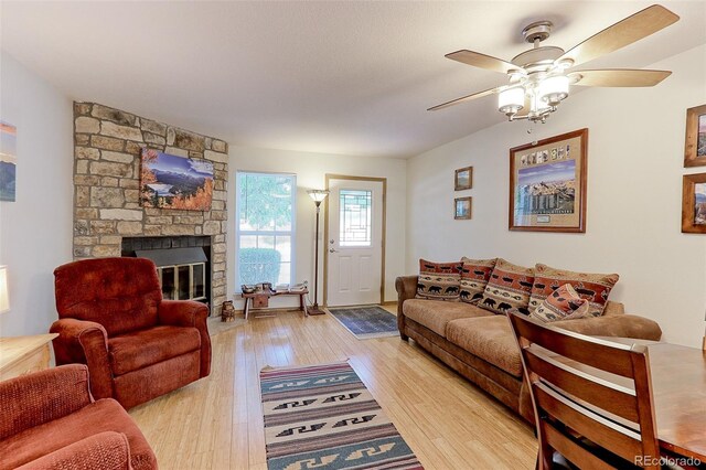 living room featuring light hardwood / wood-style flooring, ceiling fan, and a stone fireplace