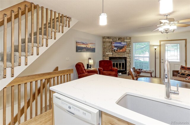 kitchen featuring white dishwasher, decorative light fixtures, sink, a stone fireplace, and ceiling fan