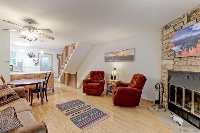 living room featuring a fireplace, a textured ceiling, ceiling fan, and light hardwood / wood-style floors