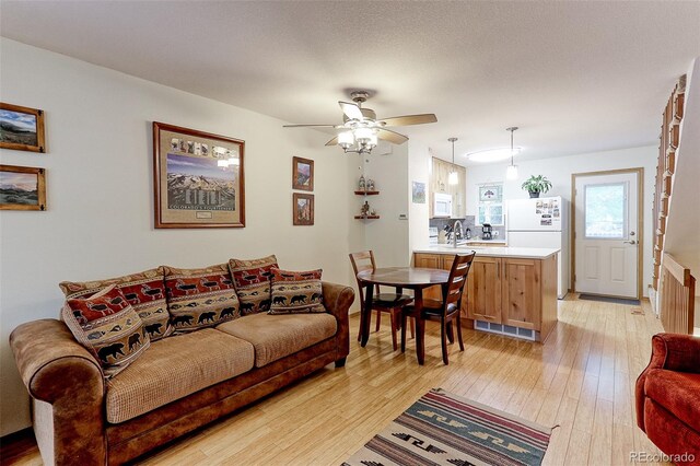 living room featuring light wood-type flooring, a textured ceiling, and ceiling fan