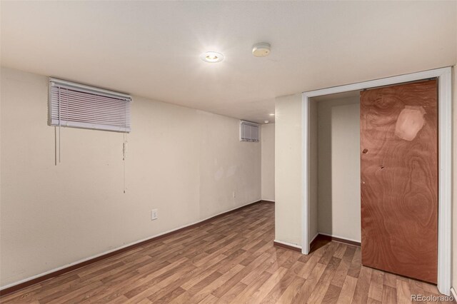 basement featuring a wall mounted air conditioner and light hardwood / wood-style flooring