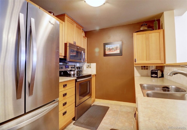 kitchen with appliances with stainless steel finishes, light countertops, a sink, and light brown cabinetry