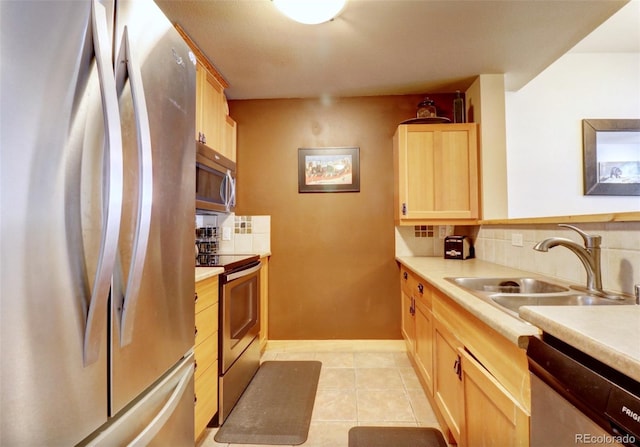 kitchen with a sink, stainless steel appliances, light countertops, light brown cabinets, and backsplash